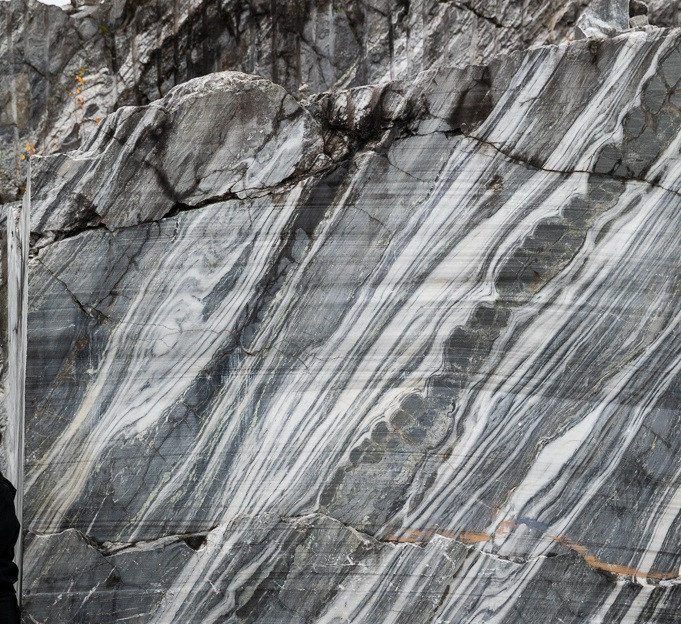 A fragment of the wall of the “Italian” quarry. The northern part of the deposit, where in the 1980s marble was mined for facing stone by rope method. A complex interlayer of steeply falling layers of calcite and dolomite marble with a boudinaged (harder) layer of dark gray in the central part, indicating a significant tectonic elaboration of marble.